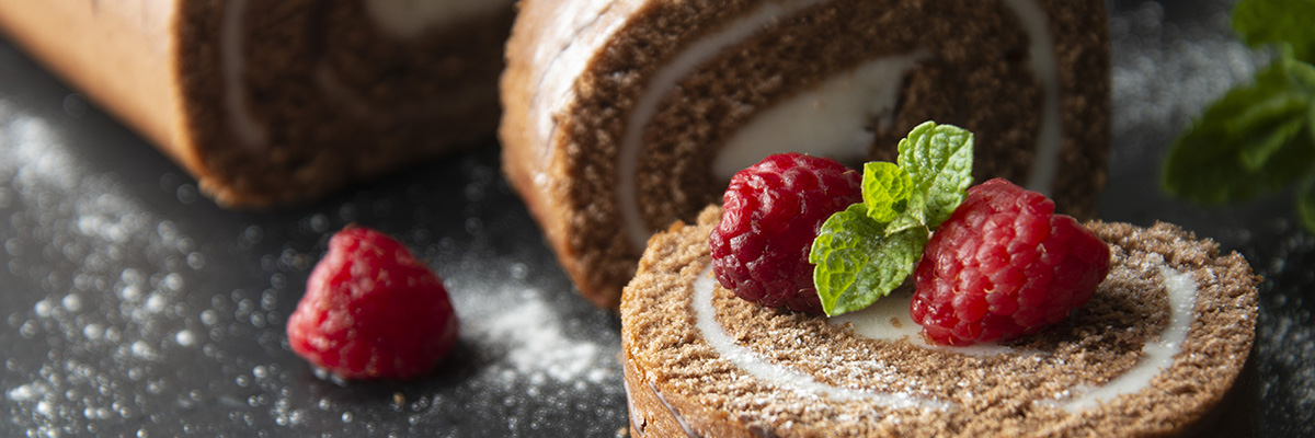 suklainen kääretorttu tomusokerilla ja vadelmilla koristeltuna
