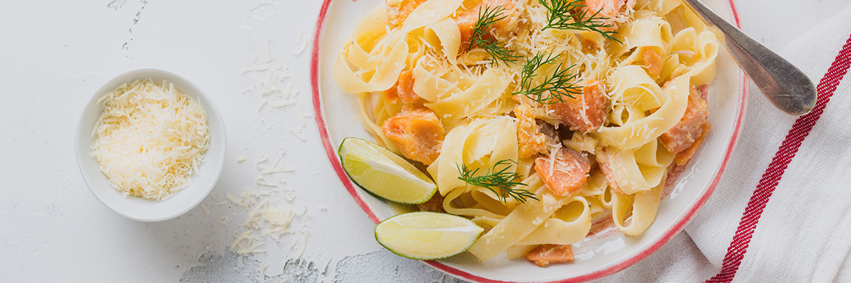 kermainen lohipasta valkoisella lautasella parmesaanin tillin ja limen kanssa