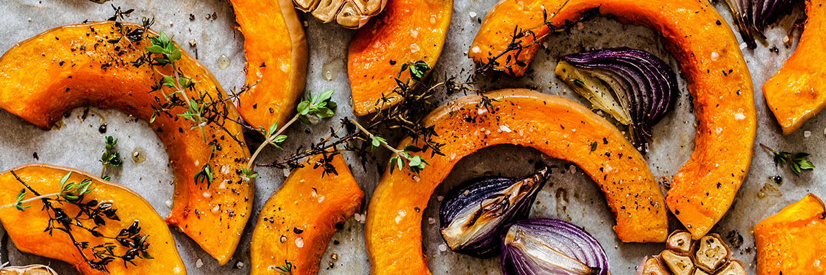 Lähikuva paahdetuista sipuleista ja yrteillä maustetuista paahdetuista myskikurpitsasiivuista 