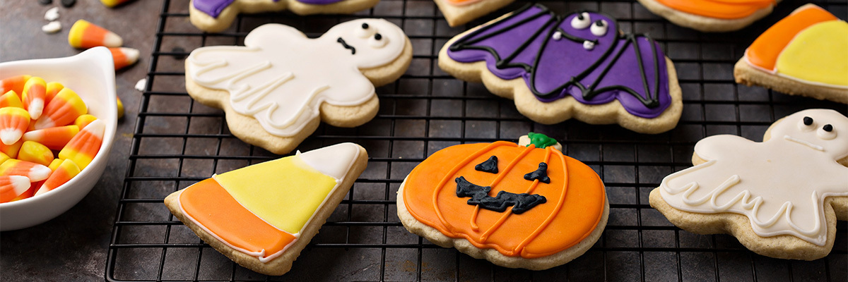 haamujen, lepakoiden ja kurpitsojen muotoisia värikkäitä halloween keksejä metalliritilällä tummalla taustalla